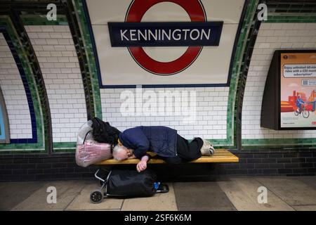Un sans-abri dort sur un banc du métro londonien à côté d'un quai de la gare de Kennington, inconscient des passagers ou du bruit des trains qui passent. Banque D'Images