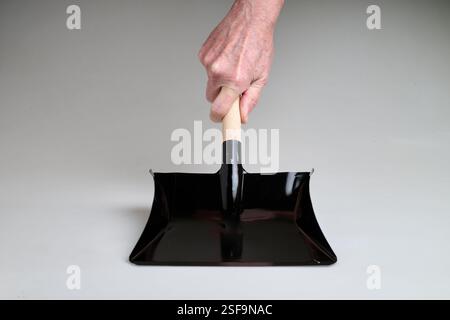 Pelle à poussière en métal noir neuve et propre tenant par la main de l'homme dans la lumière de studio sur fond blanc Banque D'Images