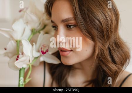 Portrait en gros plan d'une belle jeune femme sentant des orchidées de bateau blanc Banque D'Images