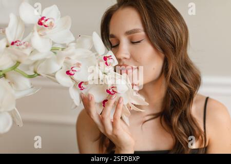 Portrait en gros plan d'une belle jeune femme assise dans un salon sentant des orchidées de bateau blanches Banque D'Images