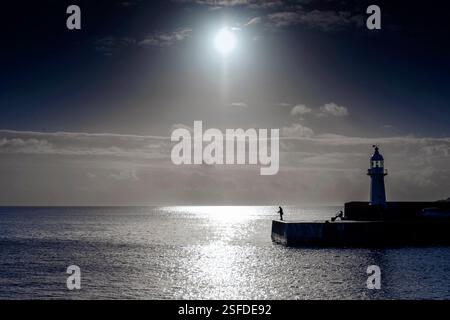 Pêcheur sur le port de mevagissey avec le phare victorien de Pier Head silhouetté contre le soleil, port de mevagissey, Cornwall Banque D'Images