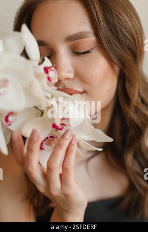 Portrait en gros plan d'une belle jeune femme tenant et sentant des orchidées blanches Banque D'Images