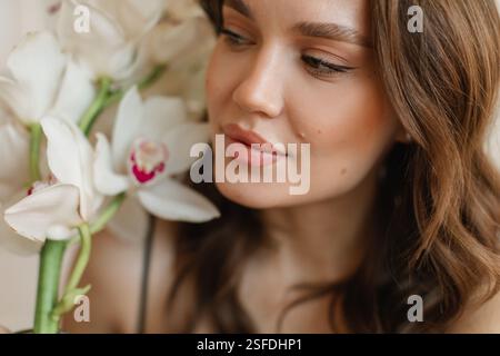 Portrait en gros plan d'une belle jeune femme tenant des orchidées blanches à côté de son visage Banque D'Images