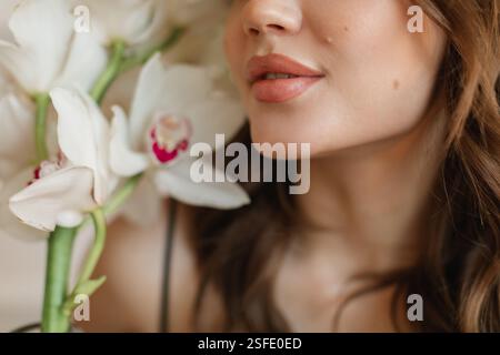 Portrait en gros plan d'une belle jeune femme tenant des orchidées de bateau blanches à côté de son visage Banque D'Images