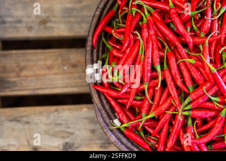Un panier tissé rempli de piments rouges vifs, placé sur une surface en bois rustique Banque D'Images