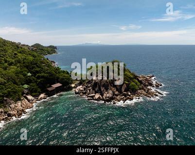 cap rocheux couvert de végétation entouré d'un océan bleu clair et de vagues s'écrasant sur le rivage. Koh Tao, Thaïlande. Banque D'Images
