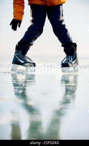 Homme athlète en veste jaune patin sur glace sur le lac gelé avec des fissures et de la neige à l'heure d'hiver. Gros plan de jambe de patin à glace Banque D'Images