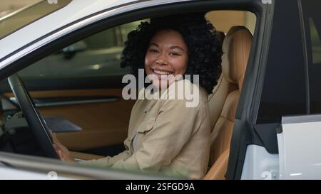Excité femme heureuse cliente afro-américaine femme d'affaires fille souriante dame à l'intérieur de la nouvelle voiture agitant la main à la caméra riant automobile électrique moderne Banque D'Images