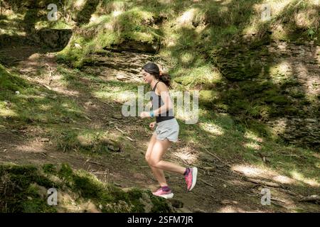 Femme faisant du jogging sur un sentier forestier, entourée de verdure luxuriante et de lumière du soleil filtrant à travers les arbres, profitant d'un style de vie actif en plein air Banque D'Images