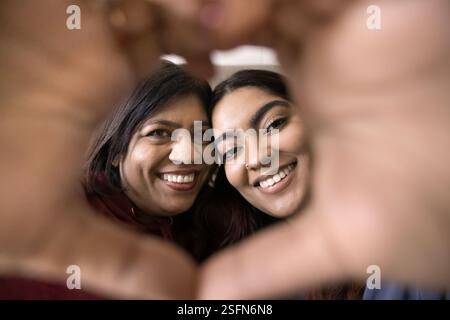 Deux femmes sourient regardent la caméra à travers la forme de coeur formée à la main Banque D'Images