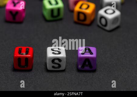 De petits cubes colorés avec des lettres de l'alphabet forment le mot 'USA' (États-Unis d'Amérique) au premier plan, fond noir, espace de copie. Banque D'Images
