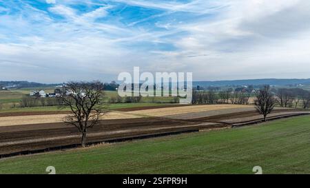 De vastes champs verts s'étendent sous un ciel bleu vif, orné de quelques nuages. À proximité, les forêts et les terres agricoles lointaines mettent en valeur les teintes automnales, créant un paysage rural serein. Banque D'Images