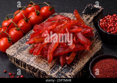 Tranches de poulet séchées, saccadées, avec saveur de cerise ou de prune, sel et épices sur un fond de béton foncé Banque D'Images