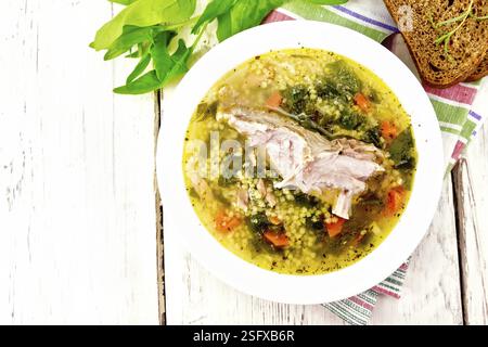 Côtes levées de porc soupe avec du couscous et les épinards dans une assiette sur du pain, serviette sur l'arrière-plan d'une planche de bois d'en haut Banque D'Images