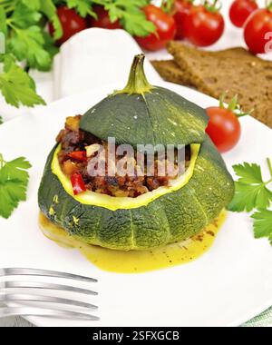 Vert courge farcie de viande, les tomates et les poivrons dans le plat, pain, ail et persil sur l'arrière-plan des panneaux en bois Banque D'Images