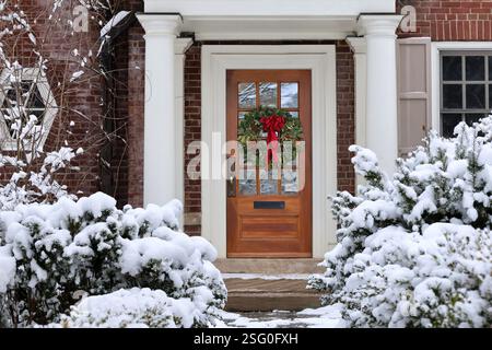 Maison de banlieue traditionnelle avec des arbustes couverts de neige et couronne décorative sur la porte d'entrée Banque D'Images