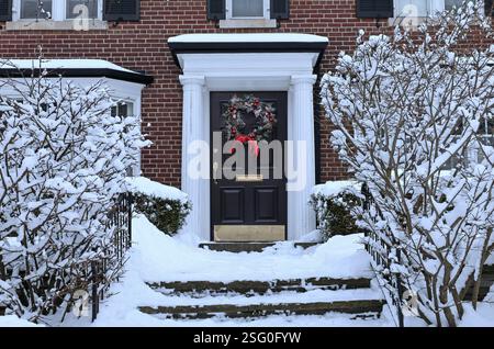 Maison de banlieue traditionnelle avec des arbustes couverts de neige et couronne décorative sur la porte d'entrée Banque D'Images