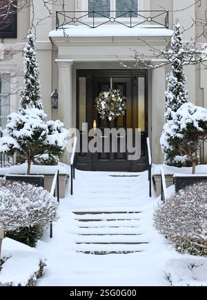 Maison de banlieue traditionnelle avec des arbustes couverts de neige et couronne décorative sur la porte d'entrée Banque D'Images