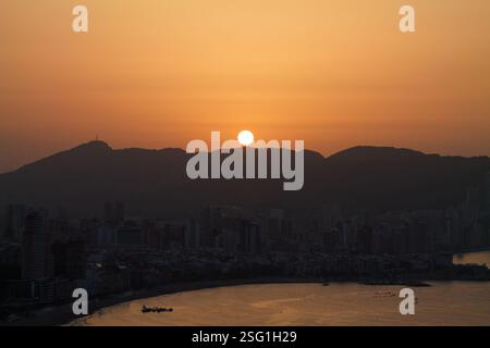Un coucher de soleil serein sur une ville côtière, avec le coucher de soleil derrière les montagnes. La ligne d'horizon comprend de hauts bâtiments et une plage calme, reflétant la chaleur d'oran Banque D'Images