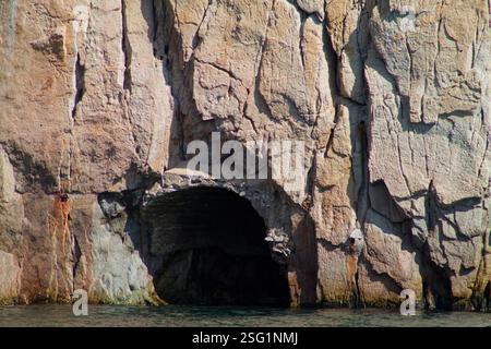 Une formation rocheuse naturelle avec une grande arche ou entrée de grotte, entourée de falaises accidentées et d'eau à la base. Banque D'Images