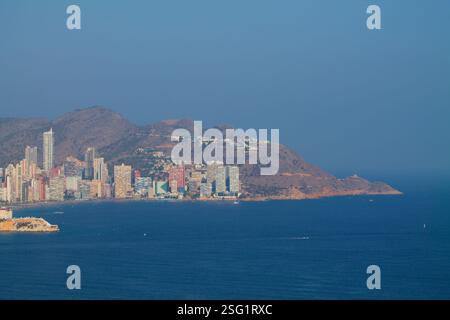 Une vue panoramique sur une ville côtière avec des gratte-ciels modernes le long du rivage, sur fond de montagnes et un ciel bleu clair. La mer est c Banque D'Images