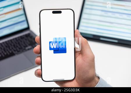 PRAGUE, TCHÉQUIE - JUILLET 2024 : logo de mot sur l'écran du smartphone dans la main de Mans et ordinateur portable sur le fond Banque D'Images