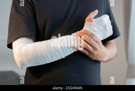 Jeune homme portant un T-shirt noir avec un bandage de gaze enroulé autour de la main de blessure. Concept de premiers soins, d'accident et de traitement des blessures. Banque D'Images