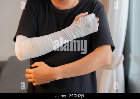 Jeune homme avec un bandage de gaze enroulé autour de ses bras blessés, main et coude à la maison. Concept de premiers soins. Banque D'Images