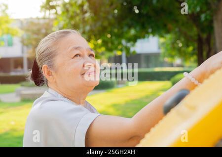 Femme asiatique senior active faisant de l'exercice des mains à l'équipement d'exercice dans le parc. Mise au point sélective. Banque D'Images