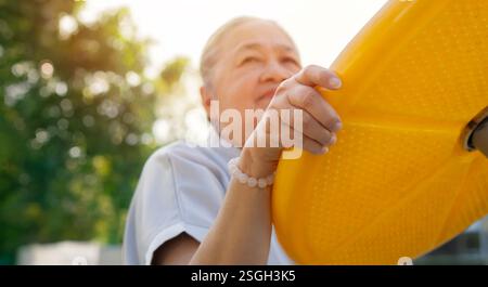 Focalisation sélective de la femme asiatique âgée qui exerce avec l'équipement d'exercice au parc le matin. Exercice à l'extérieur, espace de copie. Banque D'Images