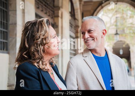 Joyeux couple d'âge mûr s'engageant dans une conversation sincère avec des sourires chaleureux et des rires partagés tout en profitant de la compagnie de l'autre dans un magnifique cadre extérieur plein de vie et d'énergie. Photo de haute qualité Banque D'Images