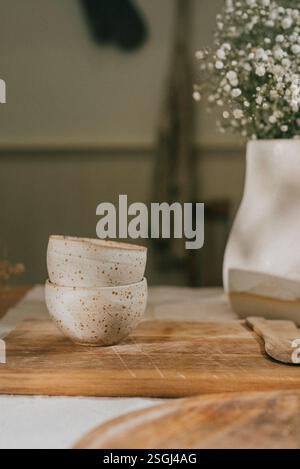 Deux bols en céramique blanche reposent sur une planche à découper en bois. Les bols sont vides et la planche à découper est posée sur une table Banque D'Images