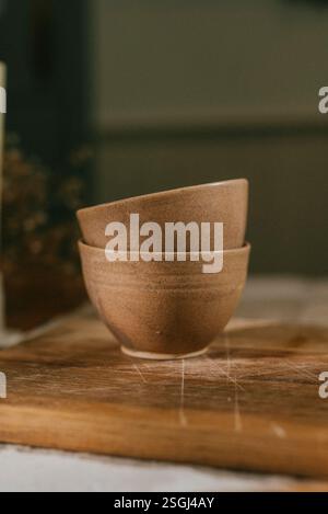 Deux bols en céramique marron sont assis sur une planche à découper en bois. Les bols sont placés à proximité les uns des autres et la planche à découper est en bois. Concept de chaleur a Banque D'Images