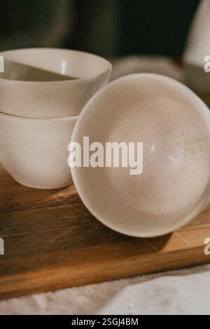 Quatre bols blancs sont assis sur une planche à découper en bois. Les bols sont tous de tailles différentes et sont disposés en rangée. La planche à découper en bois est le b. Banque D'Images