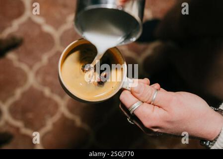 Une personne verse du lait dans une tasse de café. Le café est chaud et le lait est versé lentement Banque D'Images