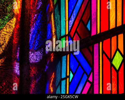 Une image abstraite en gros plan d'un vitrail dans une église médiévale avec des motifs de lumière, d'ombre et de couleur se reflétant sur le mur Banque D'Images