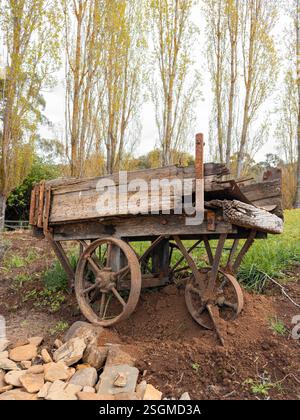 Vieux chariot en bois vieilli dans un cadre de ferme rustique avec de grands arbres Banque D'Images