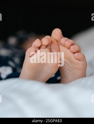 Les pieds d'un petit enfant dans le lit d'un parent sur des draps blancs roulés dans une couverture blanche . Photo de haute qualité Banque D'Images