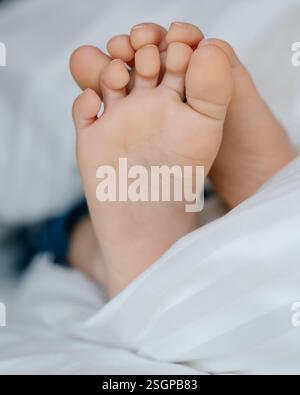 Les pieds d'un petit enfant dans le lit d'un parent sur des draps blancs roulés dans une couverture blanche . Photo de haute qualité Banque D'Images