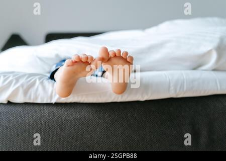 Les pieds d'un petit enfant dans le lit d'un parent sur des draps blancs roulés dans une couverture blanche . Photo de haute qualité Banque D'Images