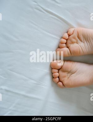 Les pieds d'un petit enfant dans le lit d'un parent sur des draps blancs roulés dans une couverture blanche . Photo de haute qualité Banque D'Images