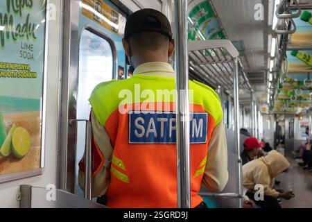 Jakarta, Indonésie - 8 février 2024 : agent de sécurité de la ligne de banlieue dans un wagon, debout devant la porte du train. Banque D'Images