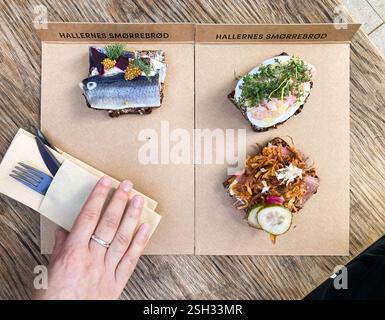 Photographie regardant vers le bas sur 3 sandwichs ouverts sur des feuilles de carton, avec « HALLERNES Smørrebrød » écrit en haut des deux. Les sandwichs sont du poisson ; oeuf Banque D'Images
