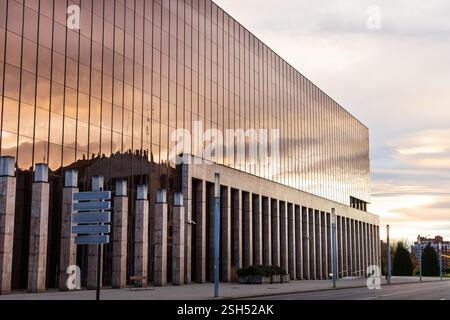 Un bâtiment moderne en verre, Oficina General de Información y Atención (OIAC) au coucher du soleil, avec le ciel et les nuages se reflétant sur sa surface. León, Espagne. Banque D'Images