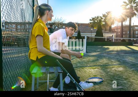 Deux jeunes joueurs de tennis font une pause sur un banc après leur match de tennis par une journée ensoleillée Banque D'Images