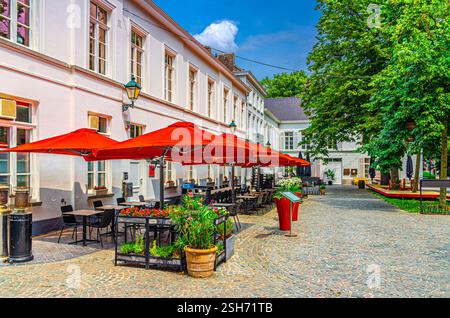 Restaurant de rue avec tables, chaises et parasols près de l'ancien bâtiment dans la cour pavée en pierre dans le centre historique de la ville de Kortrijk dans la journée ensoleillée d'été, Banque D'Images