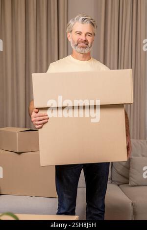 Homme barbu senior heureux emballant des boîtes en carton pendant la relocalisation Banque D'Images
