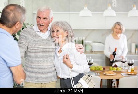 Deux couples de personnes âgées se accueillent chaleureusement alors qu'ils se réunissent pour un dîner festif de vacances à la maison Banque D'Images