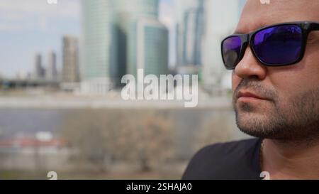 Gars brutal dans des lunettes de soleil sur le fond de la ville. Brutal Guy sur le fond de bâtiments à Moscou. Portrait d'homme brutal dans des lunettes de soleil en t Banque D'Images