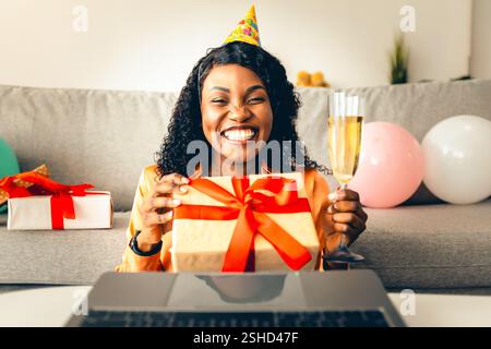Vue de face d'une femme noire offrant un cadeau d'anniversaire à un ordinateur portable à l'intérieur Banque D'Images